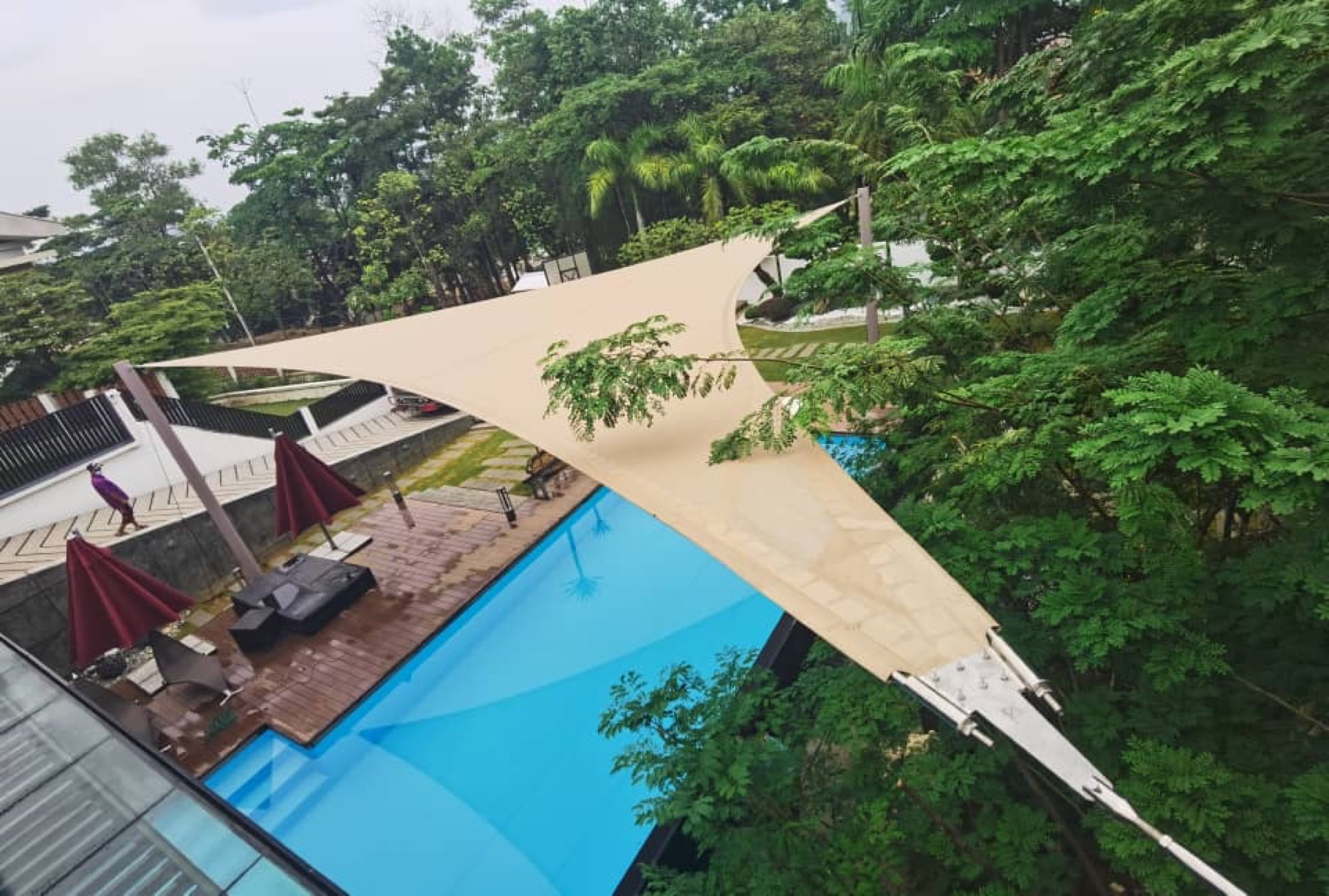 Shade sail tegangan pada tiang di atas teres tepi kolam di Malaysia